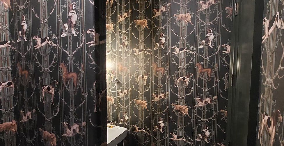 Moody powder room papered in a dark hunting-dog and antler pattern
